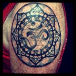 Arm tattoo in black and gray ink of an ohm symbol inside of a mandala by Natan Alexander