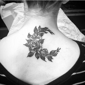 Woman showing an upper center back tattoo of roses and leaves forming a crescent moon shape in black and gray ink by Natan Alexander